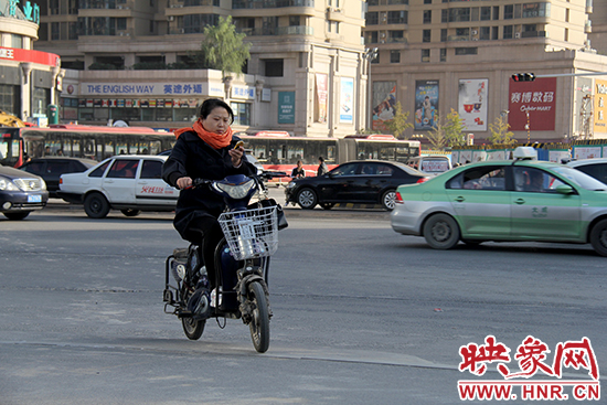 一名女士騎著電瓶車(chē)看著手機(jī)