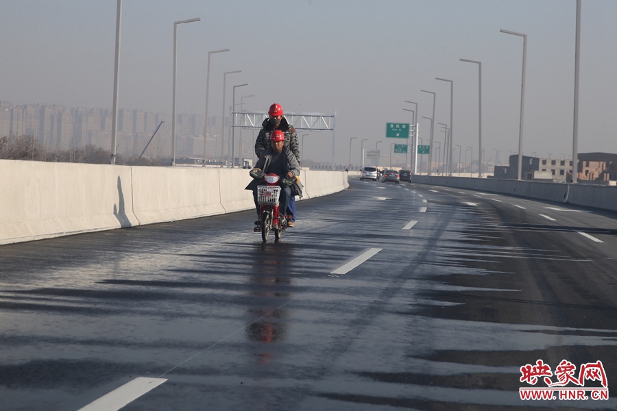 兩名工人騎車經(jīng)過灑水養(yǎng)護(hù)路面。