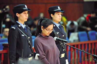 被告人盧梅低著頭，站在朝陽法院刑事審判庭的被告席上。
