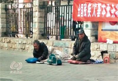 工人體育場北路，兩位乞討者路邊乞討，并輪流扮成“病人”（躺地者）。 央視截圖